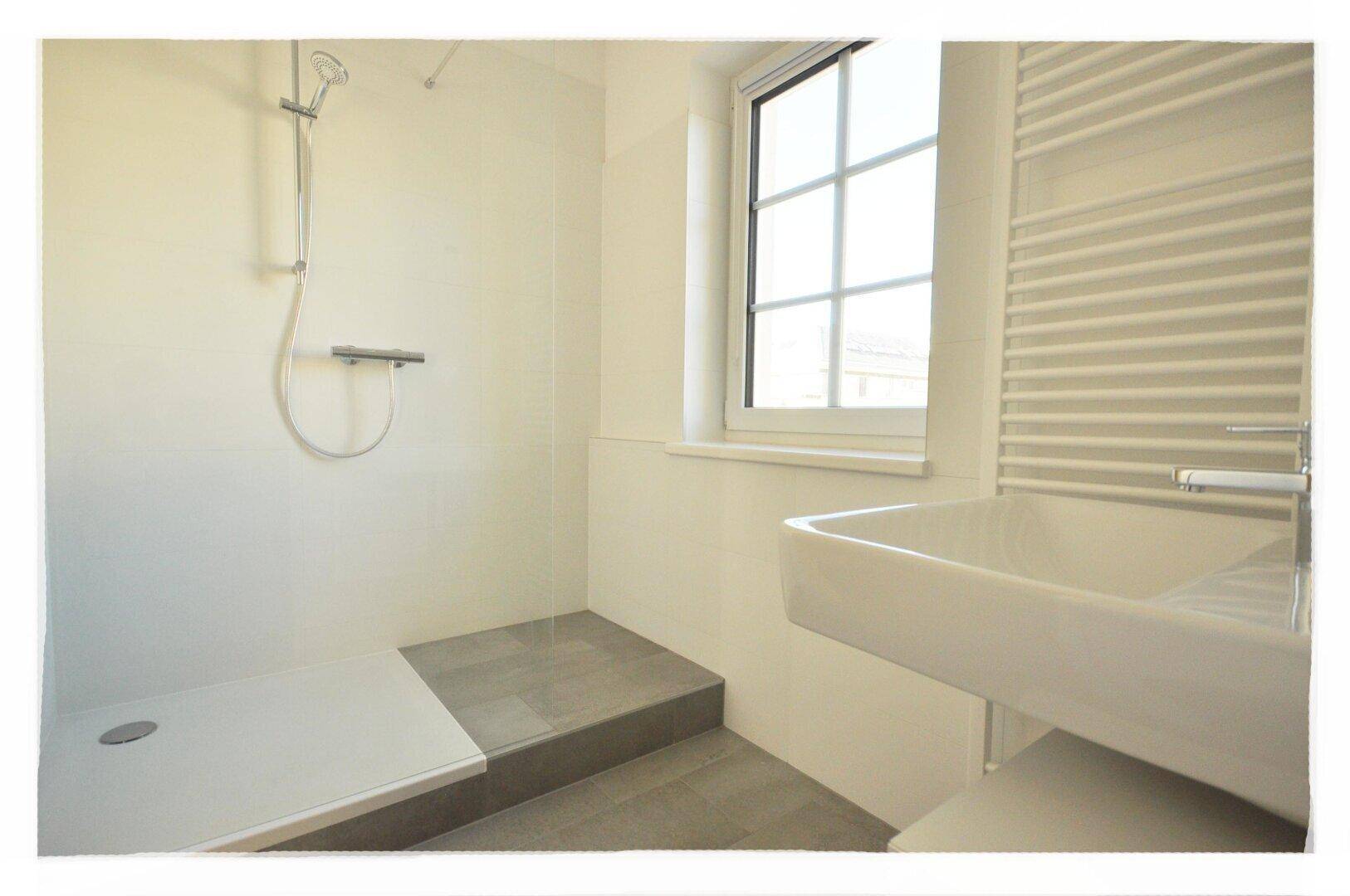 Modernes Badezimmer mit ebenerdiger Dusche, Waschbecken, Fenster und beheiztem Handtuchhalter.