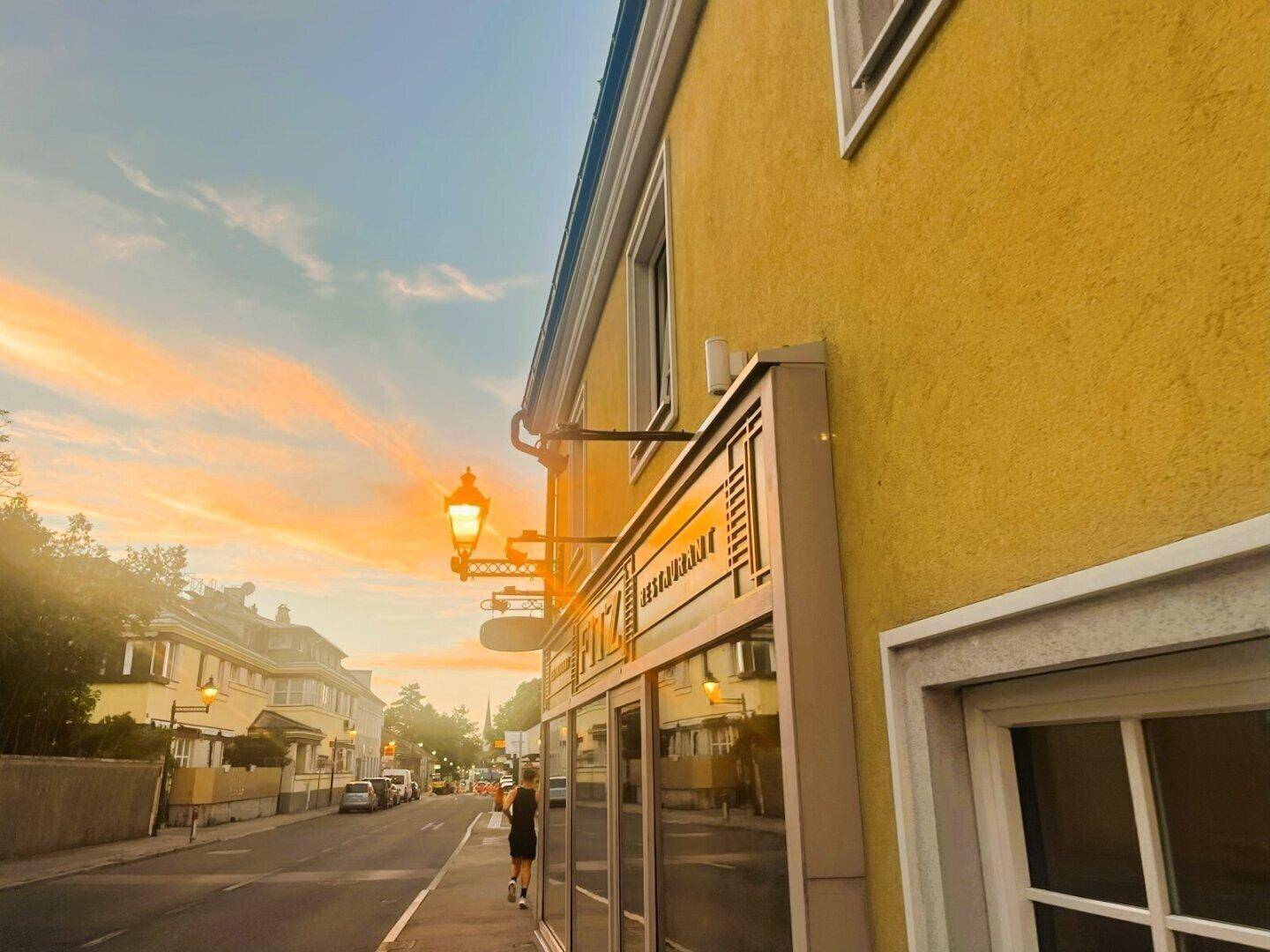 Gelbe Fassade eines Gebäudes an einer belebten Straße bei Sonnenuntergang mit warmem Licht.