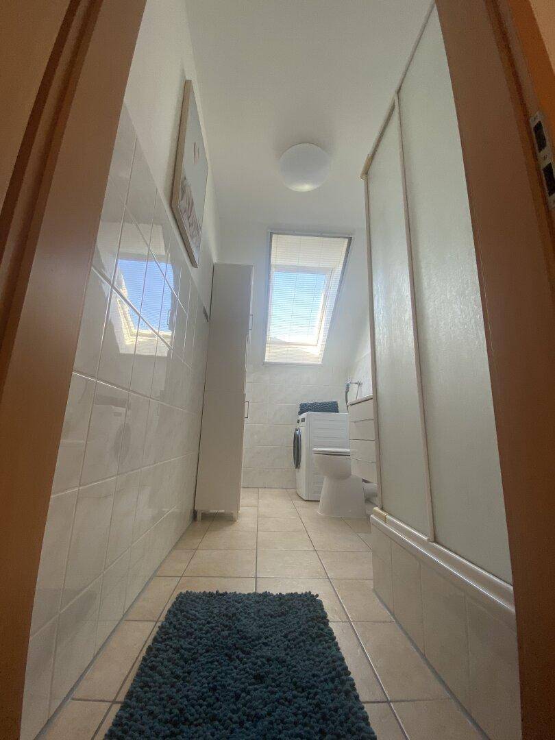 Helles Badezimmer mit Dachfenster, Dusche, WC und Waschmaschine.
