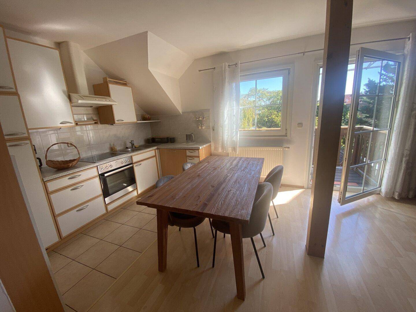 Helle Küche mit Essbereich, Dachschrägen und Zugang zu einem sonnigen Balkon.