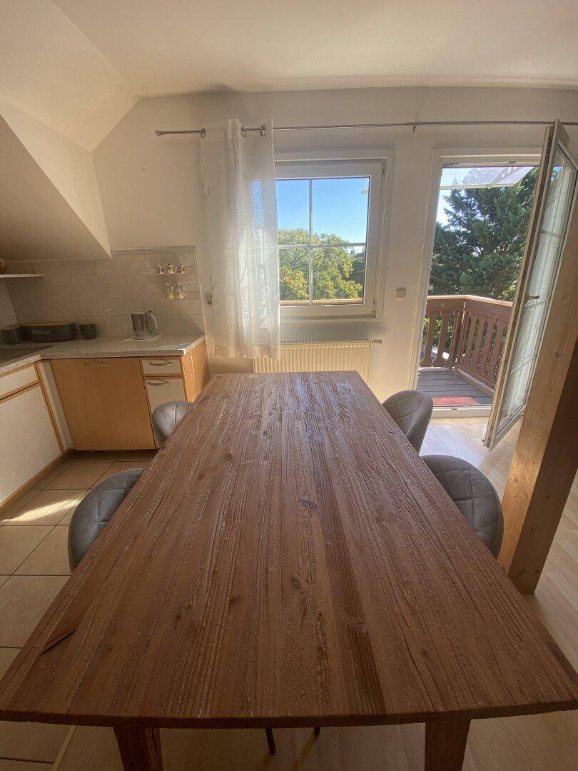 Großer Holzesstisch im hellen Essbereich mit Blick ins Grüne und Balkonzugang.