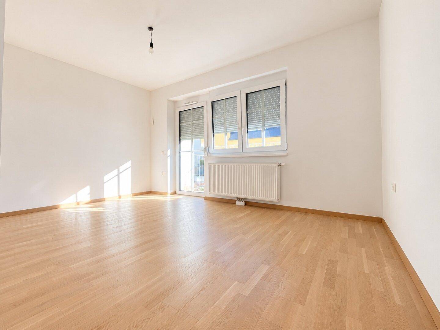 Lichtdurchfluteter Wohnbereich mit Holzboden und Zugang zu einem Balkon.