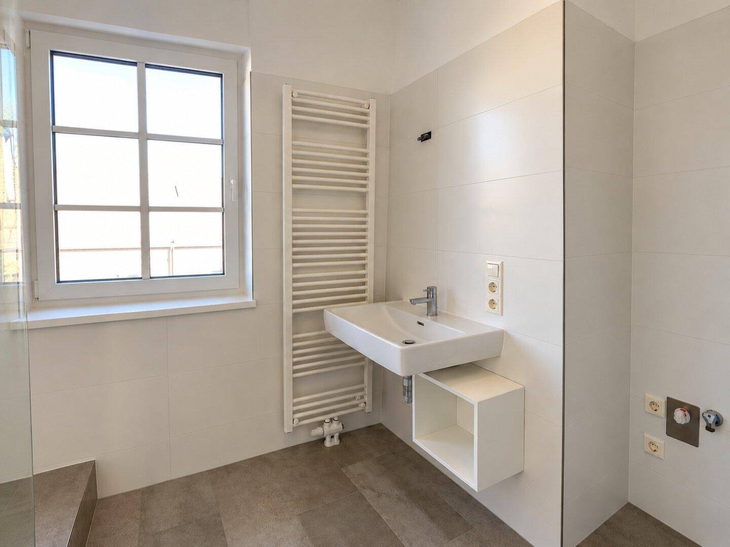 Helles Badezimmer mit modernem Waschbecken, Handtuchheizkörper und Fenster.