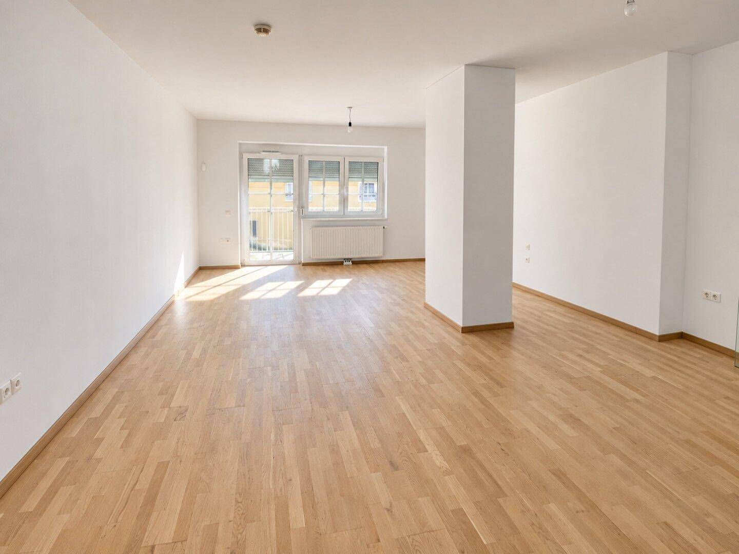 Weitläufiger Wohnbereich mit Parkettboden und viel Tageslicht durch die Balkontür.