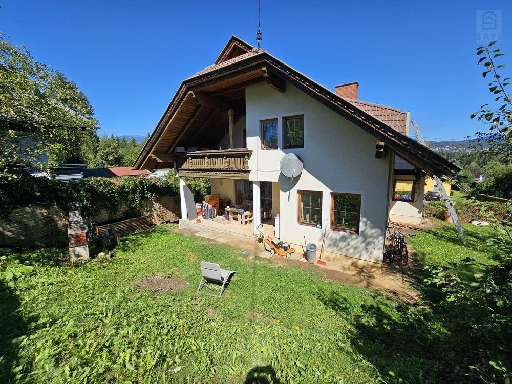Freistehendes Haus mit Satteldach, Balkon und großem Gartenbereich unter blauem Himmel.