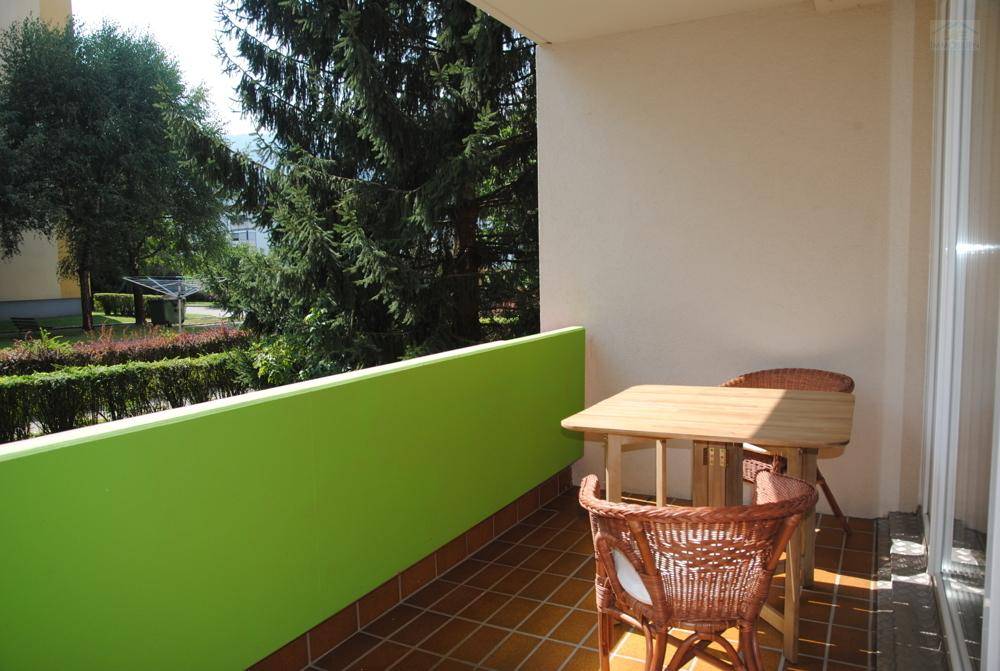 Sonniger Balkon mit Terrakotta-Fliesen, grüner Brüstung und Sitzgelegenheiten im Freien.