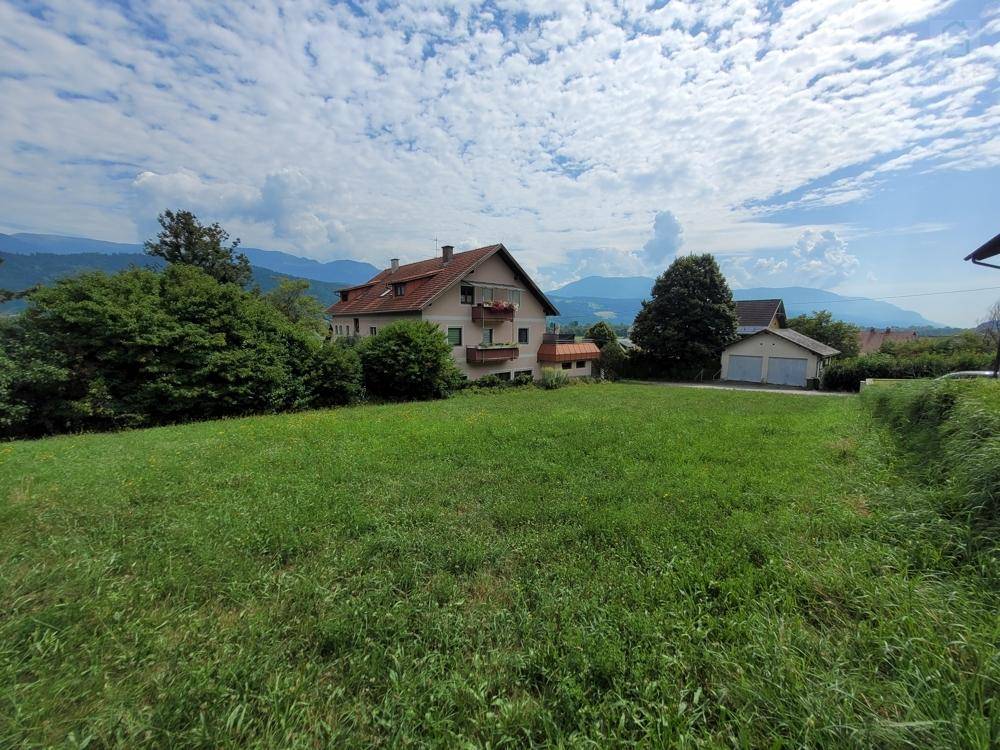 Weitläufiges grünes Grundstück mit einem traditionellen Haus und malerischem Bergblick.