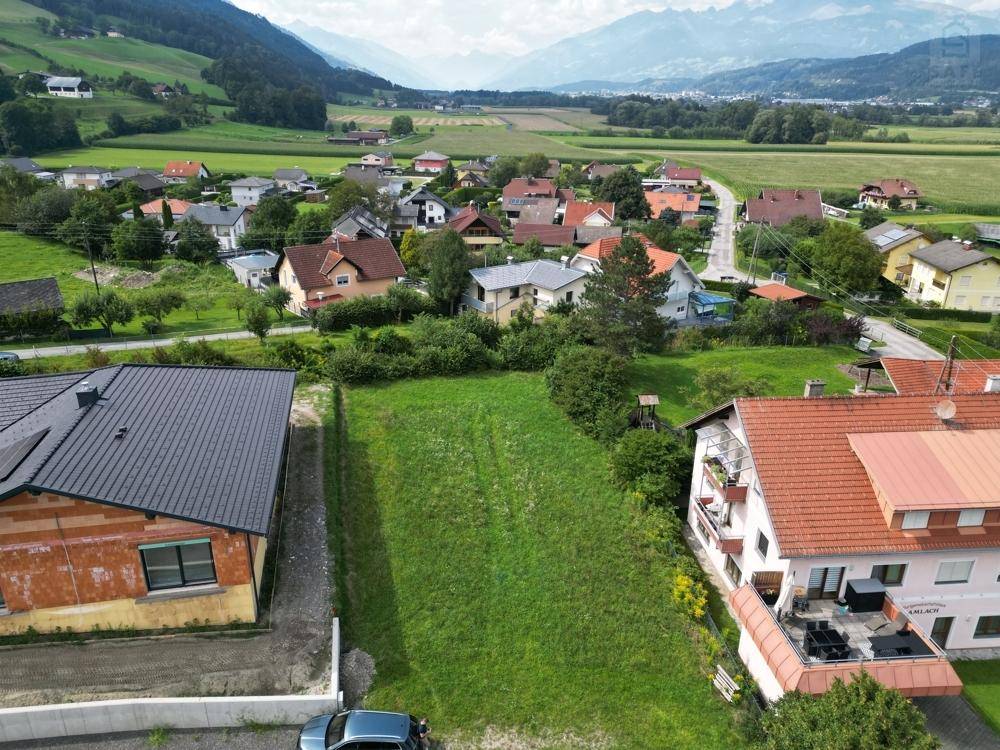 Grünes Baugrundstück mit Blick auf ein Dorf und die umliegende Berglandschaft.