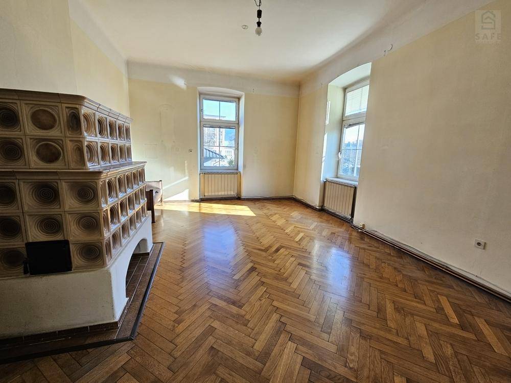 Helles Wohnzimmer mit traditionellem Kachelofen, Fischgrätparkett und großen Fenstern, die den Raum erhellen.