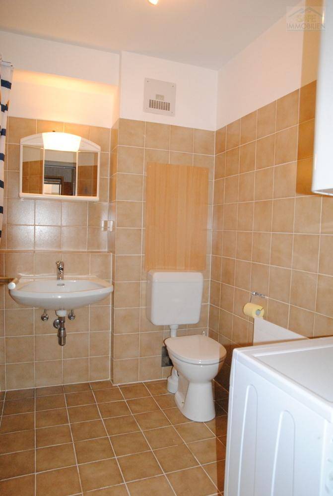 Gefliestes Badezimmer mit WC, Waschbecken und Platz für eine Waschmaschine.