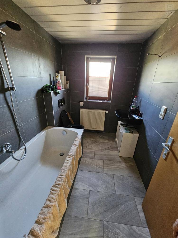 Modernes Badezimmer mit dunklen Fliesen, Badewanne und Fenster für Tageslicht.