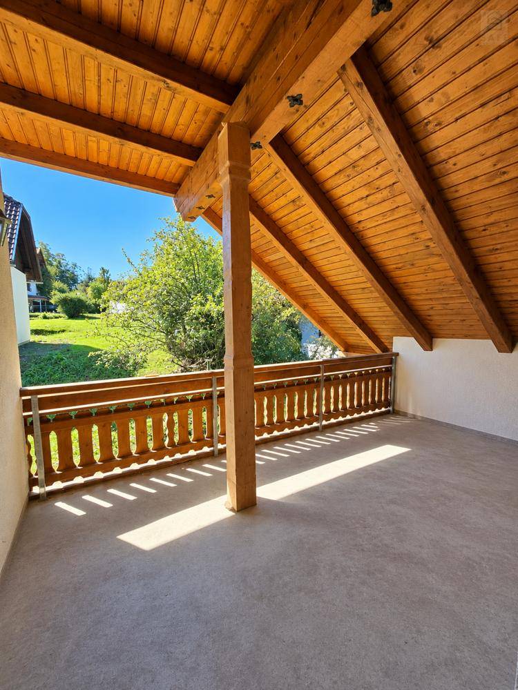 Überdachter Balkon mit Holzbalken, Holzgeländer und weitem Blick ins Grüne.