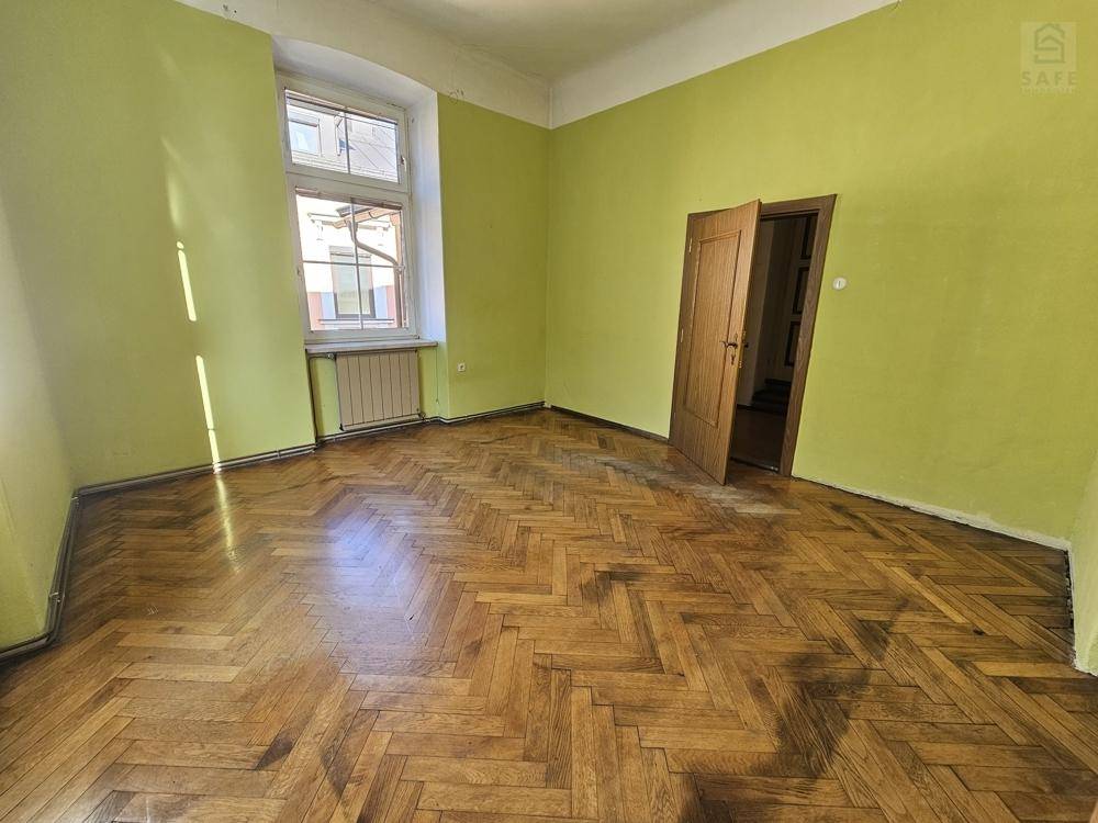 Leeres Zimmer mit auffälligen lindgrünen Wänden, klassischem Fischgrätparkett und einem Fenster mit Heizkörper.