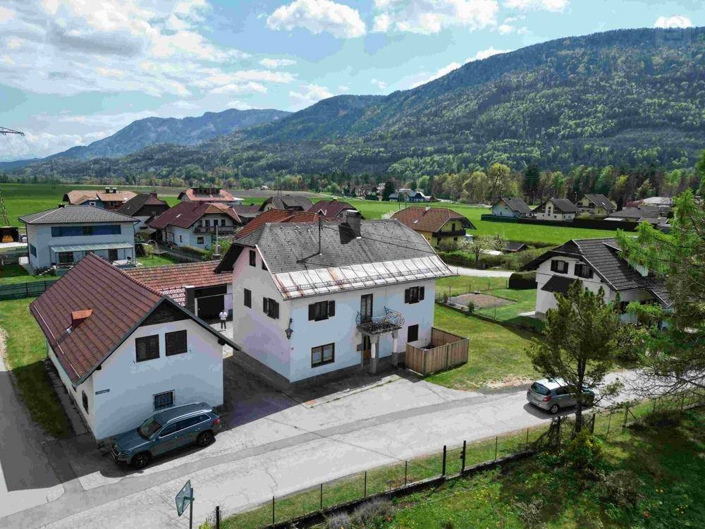 Luftaufnahme des Hauses mit umliegenden Gebäuden und grüner Berglandschaft im Hintergrund.