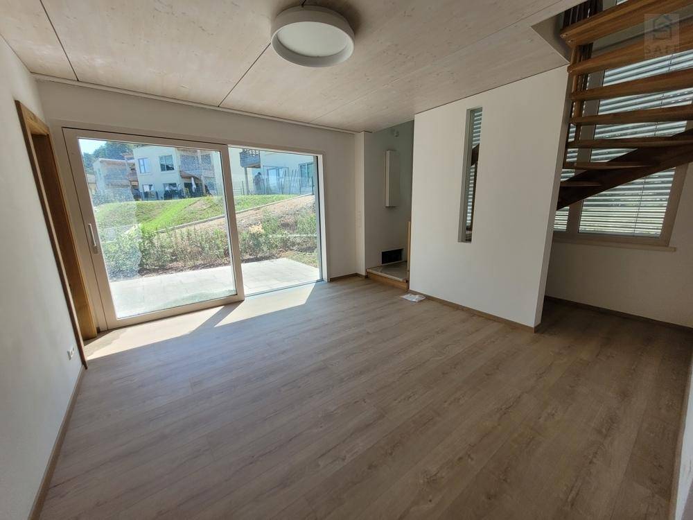 Helles Wohnzimmer mit Holzboden, großen Schiebetüren und offener Holztreppe zum Obergeschoss.