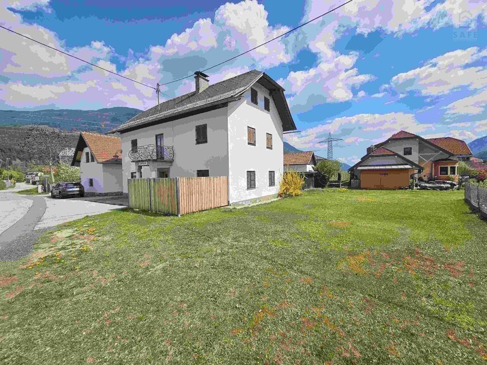 Seitenansicht eines weißen Hauses mit Satteldach und einem großen Rasenbereich im Vordergrund.