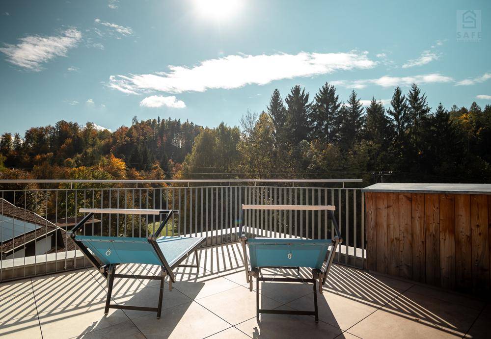Sonnige Dachterrasse mit Liegestühlen und weitem Blick auf bewaldete Hügel und den Himmel.