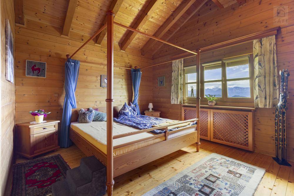 Gemütliches Schlafzimmer mit Himmelbett, Holzvertäfelung und Bergblick durch das Fenster.