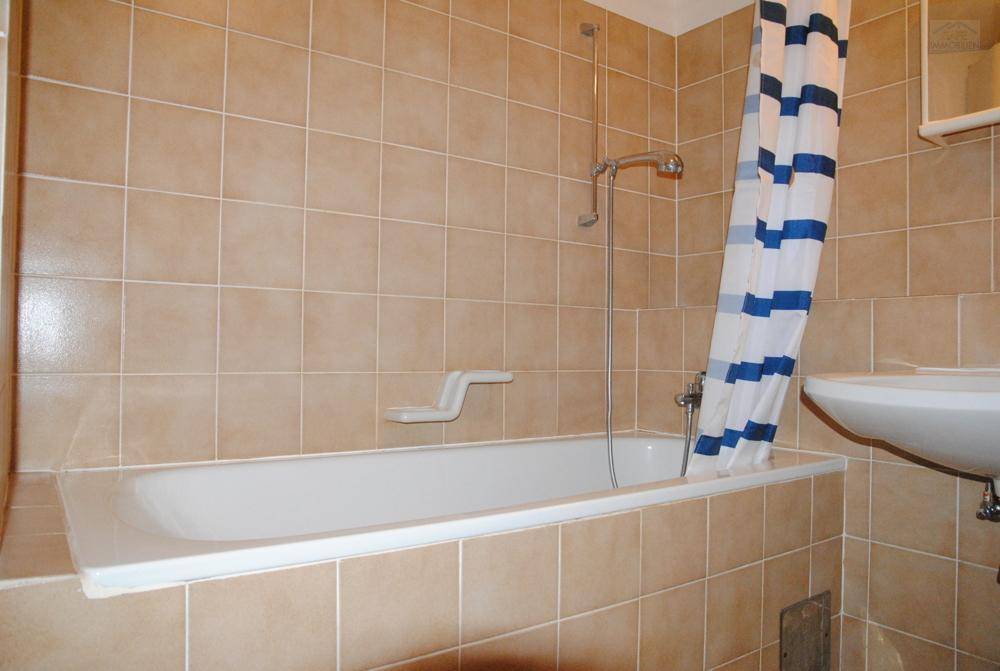Badezimmer mit Badewanne, Duschvorhang und beigefarbenen Fliesen an Wänden und Boden.