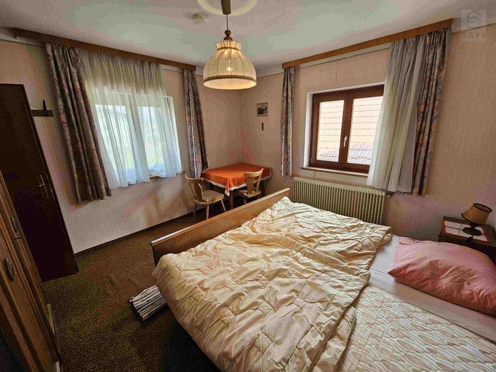 Schlafzimmer mit Einzelbett, grünem Teppichboden und einem kleinen Tisch am Fenster.
