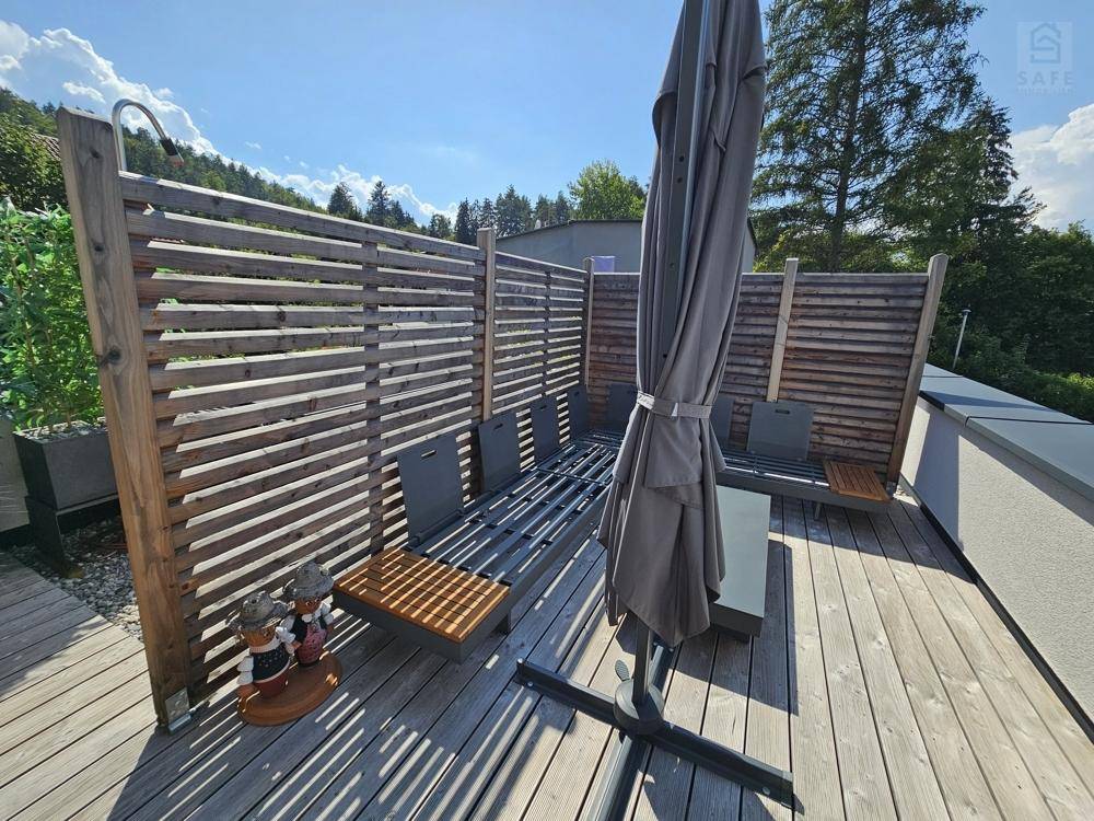 Geräumige Dachterrasse mit Holzbelag, Sonnenliegen und Sonnenschirm für entspannte Stunden.