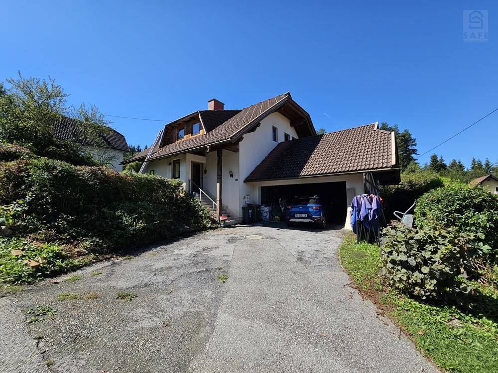 Einfamilienhaus mit Zufahrt, Carport und umgebender Hecke an einem sonnigen Tag.