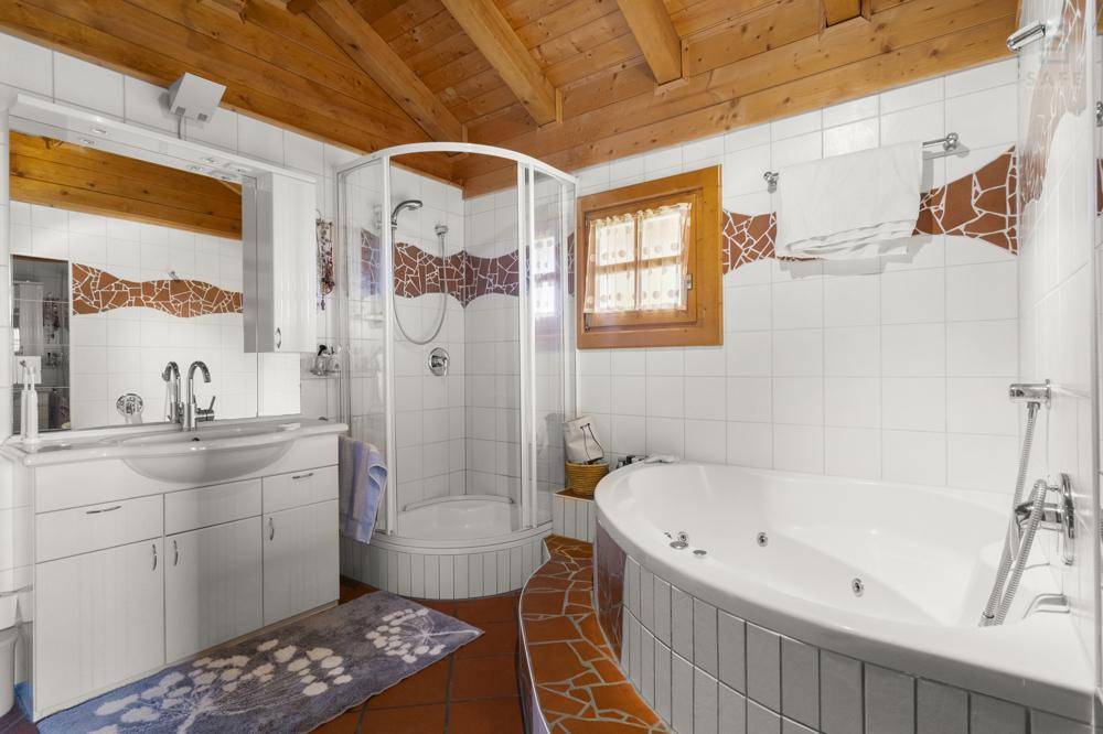 Badezimmer mit Duschkabine, Eck-Whirlpool und Fliesenboden in warmen Farbtönen.