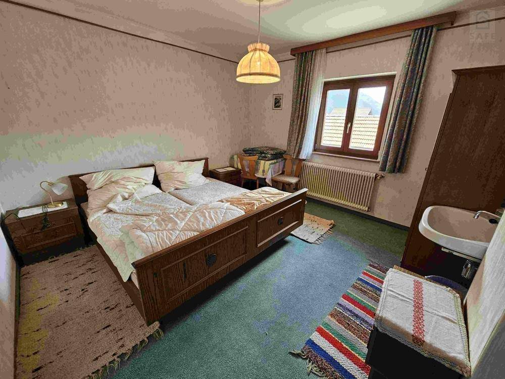 Schlafzimmer mit Doppelbett, Teppichboden und kleinem Waschbecken, in traditionellem Stil.