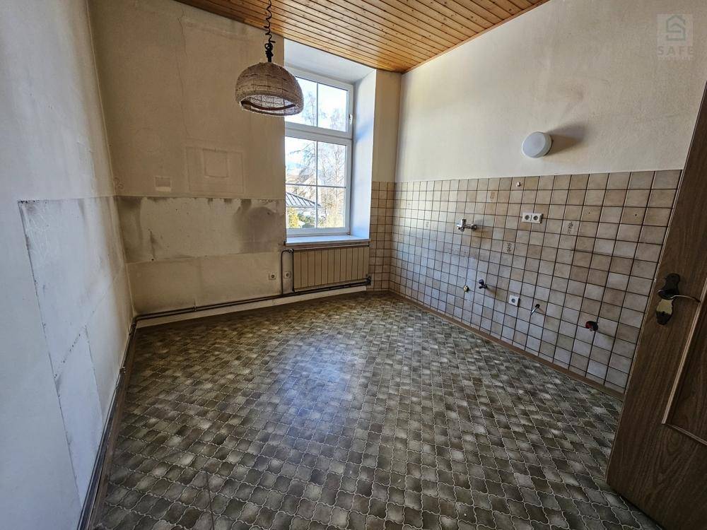 Unrenovierte Küche mit gemustertem Vinylboden, gefliestem Spritzschutz und einer Holzlamellendecke, bereit zur Neugestaltung.