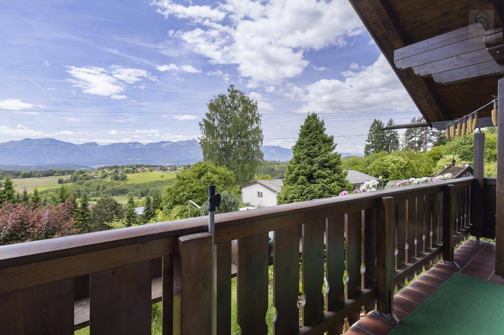 Balkon mit Holzbalkon und weitem Blick über die grüne Landschaft und die Berge unter blauem Himmel.