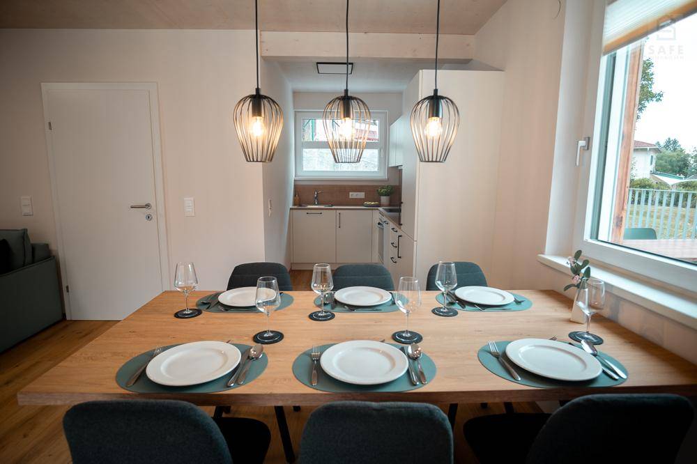 Essbereich mit großem Holztisch und moderner Beleuchtung, angrenzend an eine kompakte Küchenzeile.