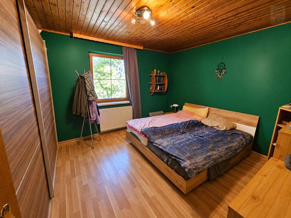 Schlafzimmer mit grünen Wänden, Holzbett, Holzdecke und Parkettboden.