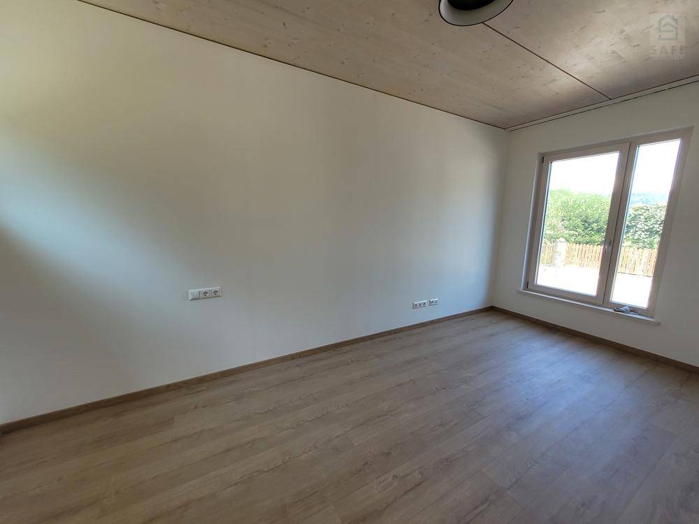 Helles Schlafzimmer mit Holzboden und großem Fenster, das viel Tageslicht hereinlässt.