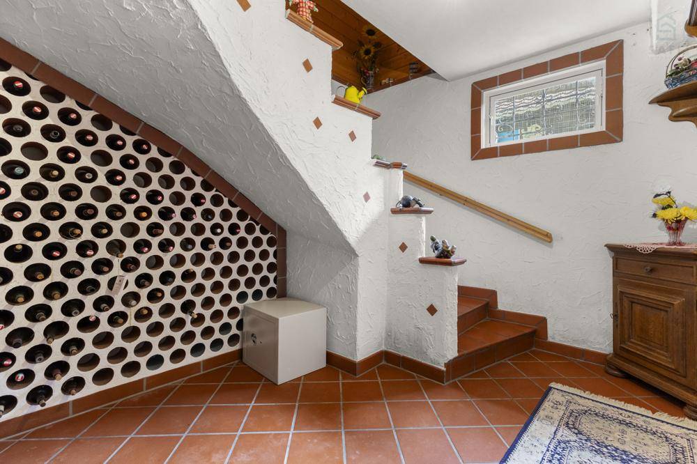 Rustikaler Weinkeller mit integriertem Weinregal und Terrakotta-Fliesenboden unter der Treppe.