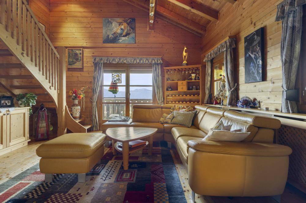 Gemütliches Wohnzimmer im alpinen Stil mit Holzvertäfelung, Ledersofa und Bergblick durch das Fenster.