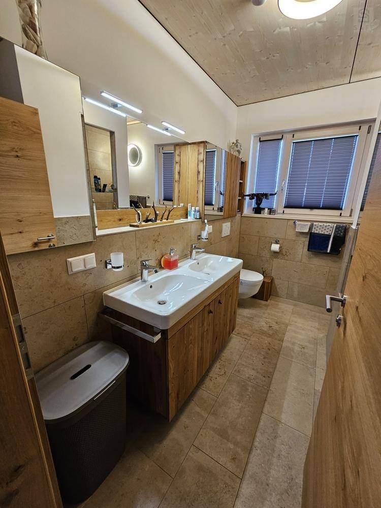Modernes Badezimmer mit Doppelwaschbecken, Spiegelschrank und Hänge-WC in heller Fliesenoptik.