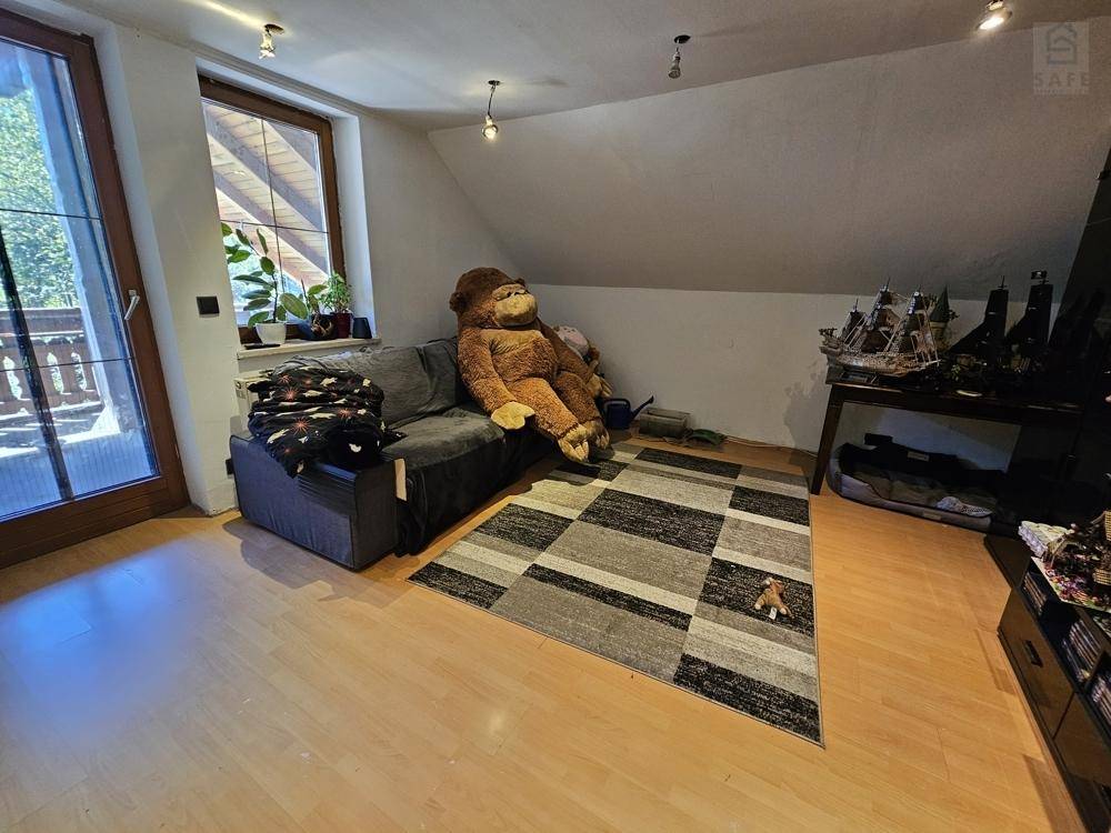 Gemütlicher Wohnbereich im Dachgeschoss mit Sofa, Holzboden und Zugang zum Balkon.