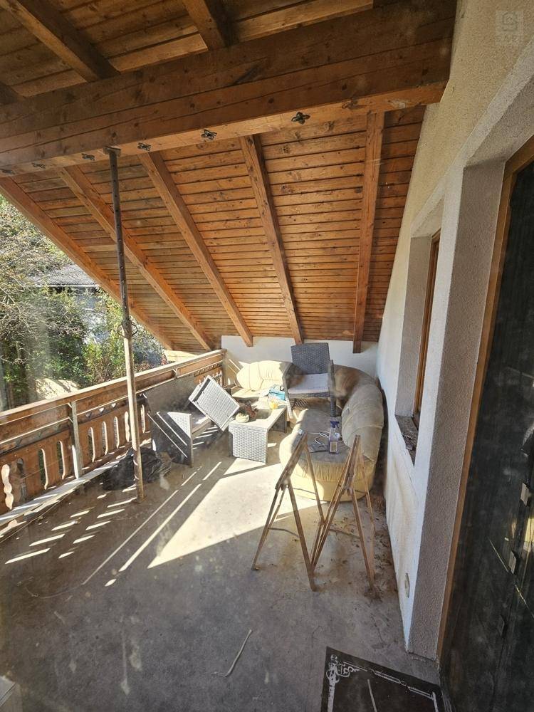 Überdachter Holzbalkon mit rustikalem Geländer und Sitzgelegenheiten, ideal für sonnige Tage.
