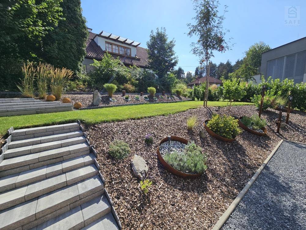 Attraktiver Garten mit Steinstufen, Mulchbeeten und dekorativen Pflanzen in sonniger Lage.