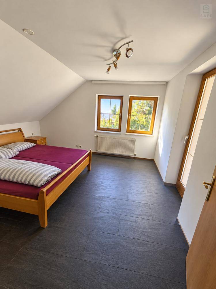 Helles Schlafzimmer im Dachgeschoss mit Doppelbett, dunklem Fliesenboden und Fenstern.