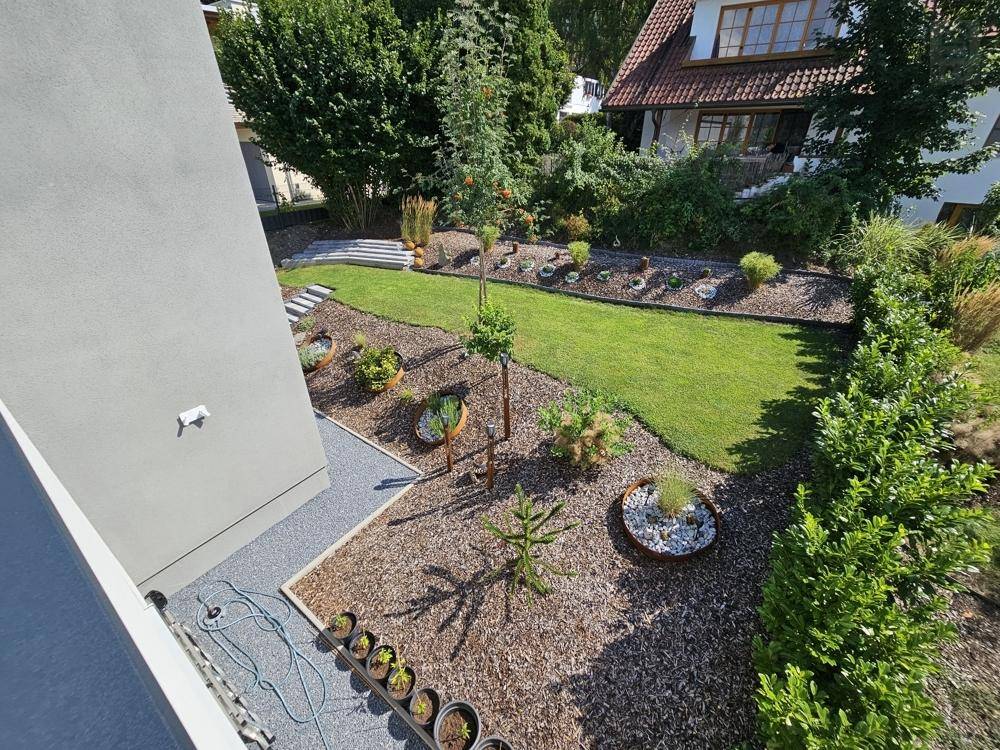 Gepflegter Garten mit Rasenflächen, Zierpflanzen und dekorativen Beeten von oben betrachtet.