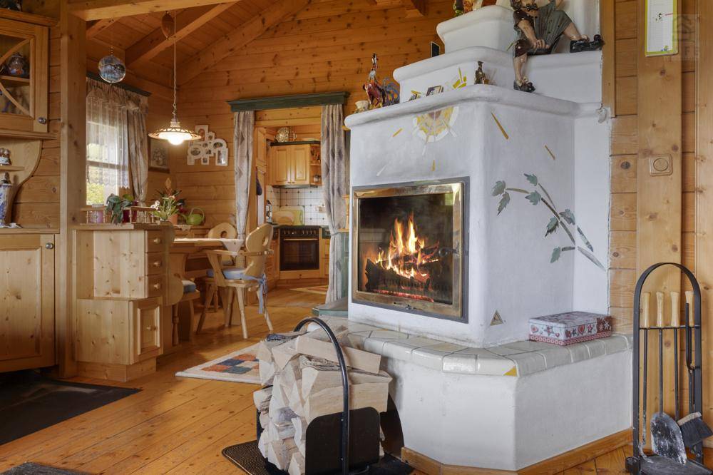 Traditioneller Kachelofen im offenen Wohn-Essbereich mit Holzboden und Blick in die Küche.