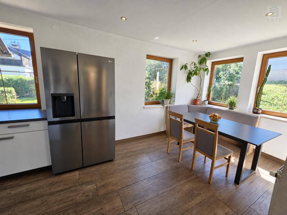 Geräumige Küche mit Essbereich, großem Kühlschrank und Blick ins Grüne durch mehrere Fenster.