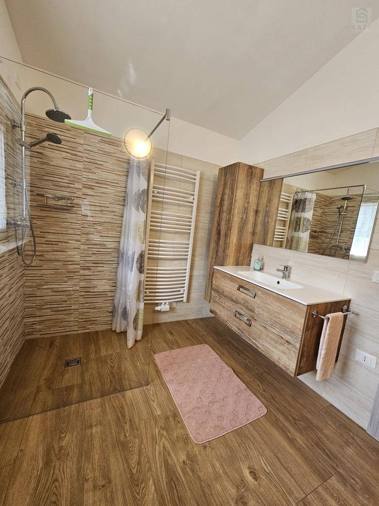 Modernes Badezimmer mit ebenerdiger Dusche, Holzoptikfliesen und beheiztem Handtuchhalter.