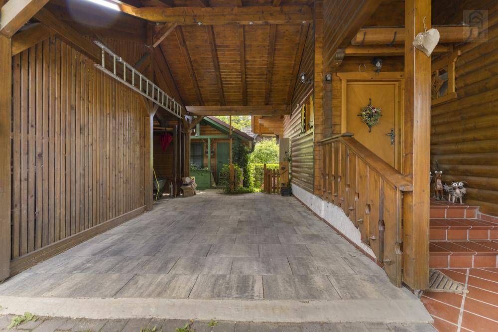 Überdachter Parkplatz oder Carport neben dem Hauseingang mit Holzverkleidung und gepflastertem Boden.