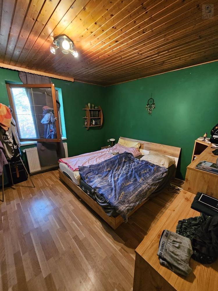 Gemütliches Schlafzimmer mit grünen Wänden, Holzbett, Holzdecke und Parkettboden.