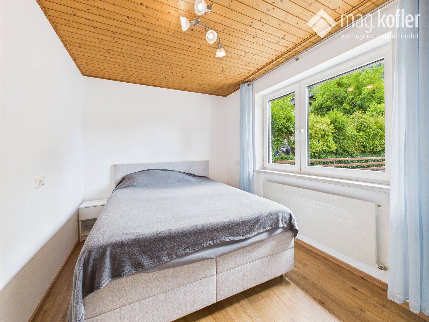 Gemütliches Schlafzimmer mit Holzdecke, Doppelbett und Fenster mit Blick ins Grüne.