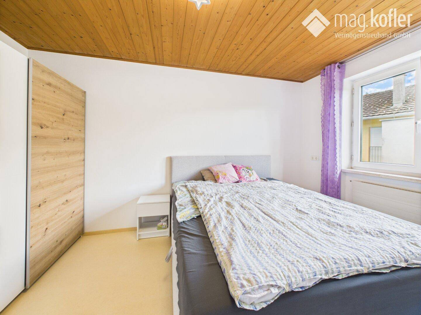 Schlafzimmer mit Doppelbett, Holzdecke und Einbauschrank in hellem Holzton.