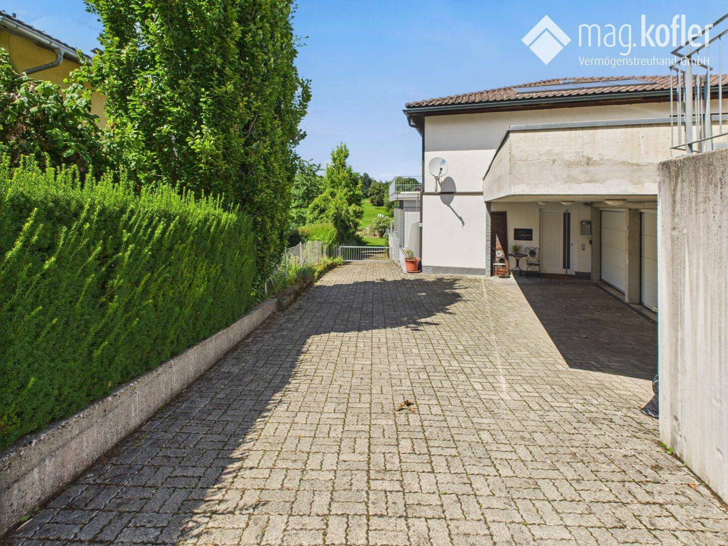 Gepflasterte Zufahrt führt zu einer Garage mit Blick auf die grüne Umgebung.