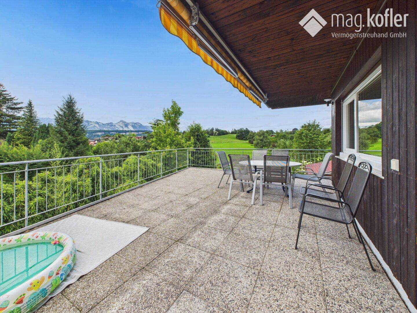 Große Sonnenterrasse mit Gartenmöbeln, Markise und weitem Blick auf die Berge und Landschaft.